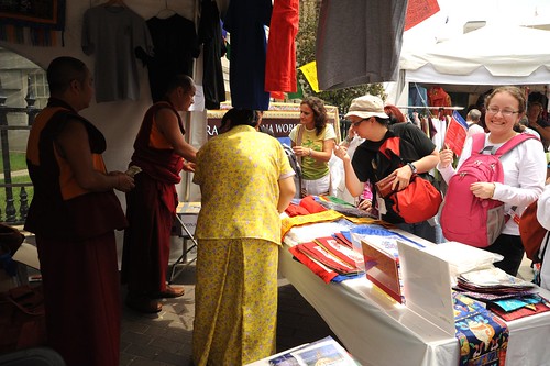 Monks working their booth, Tibetan woman in forground is wearing a two piece patterned yellow Tibetan chuba of contemporary design, tent market, Kalachakra for World Peace, Happy Birthday to the Dalai Lama Parade, Washington D.C., USA by Wonderlane