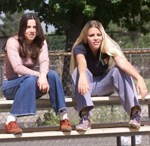 Lindsay and Kim, a white teenage girl with blond hair, sit on the bleachers