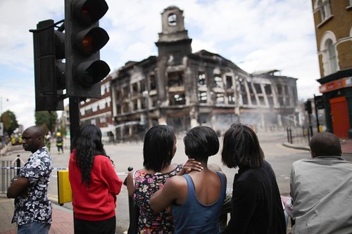 Residents watch as a building burns during a youth rebellion which erupted on Tottenham High Road on August 7, 2011 in London, England. The unrest was sparked by a police killing of a black youth and the overall economic crisis. by Pan-African News Wire File Photos
