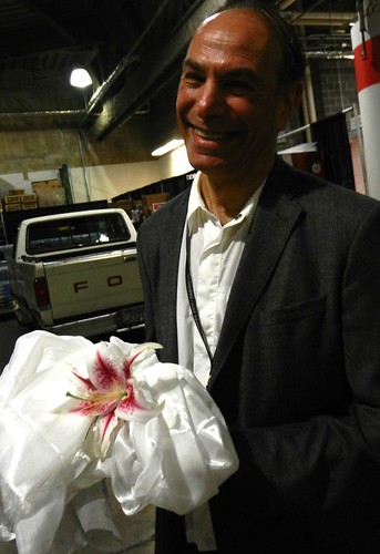 A man dressed in a suit holding a pink lily wrapped in khatas, backstage preparing for the mandala offering to His Holiness 14th Dalai Lama of Tibet, Kalachakra for World Peace, Verizon Center, Washington D.C., USA by Wonderlane
