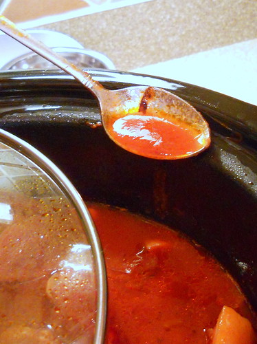 Red broth in crock pot. A metal spoon shows the broth closer up.
