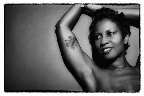 black and white photo of Essence, a black woman, smiling and leaning against a wall
