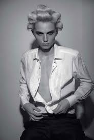 super model andrej pejic in dossier journal with hair curled on top of his head wearing an unbuttoned white shirt and dark trousers 