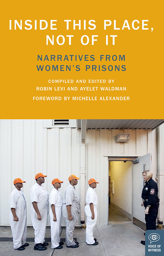 the cover of Inside This Place Not Of It. It features a scene from prison, five black women wearing white jumpsuits and orange hats. The stand single file and face a white female office in a blue uniform. Even though they are standing in subordination, there is dignity in the way they hold themselves.