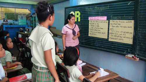 A pupil of Zapatera Elementary School (facing the blackboard) reads some ways to help manage waste while her classmates and teacher listen. (Tashuana Alemania)