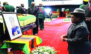 FARE THEE WELL . . . Vice-President Joice Mujuru kneels before a portrait of her late husband Retired General Solomon Mujuru and the casket containing his body at Stodart Hall in Mbare yesterday morning. by Pan-African News Wire File Photos