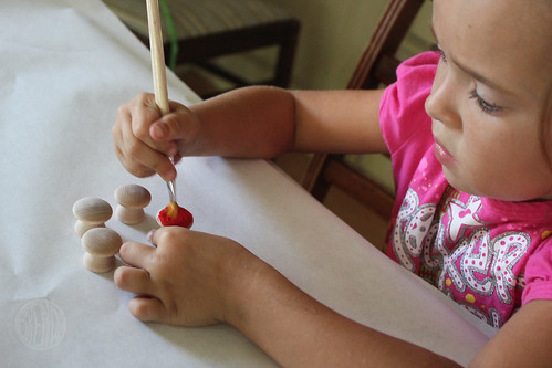 small child painting wooden knobs with red paint 