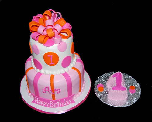 pink and orange 2 tier first birthday cake topped with a bow and smash cake