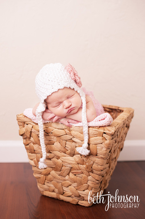 newborn baby girl in pink and white hat in basket in photography studio