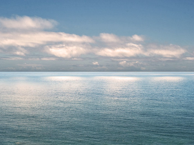 The Pacific Ocean catches the soft light of late afternoon from a cloud filled blue sky.