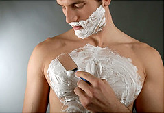young man with shaving cream on his face and chest shaving his chest hair with a disposable razor