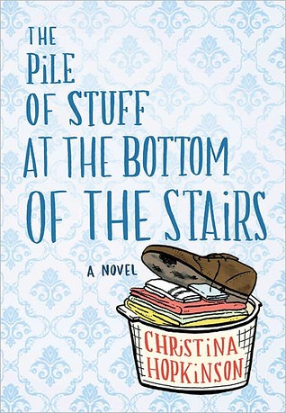 US cover: a background of pale blue and white wallpaper with the title in big, royal blue letters and a small drawing of an ivory-colored laundry basket at the bottom-right. The basket is full of neatly folded colorful shapes but has a big brown shoe thrown carelessly on top. The author's name appears in orangish-pink on the outside of the basket.