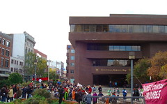 Photo de la foule où on voit le devant de la Bibliothèque Gabrielle-Roy ainsi que la bannière Charest contre les pauvres
