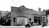 People parked in front of an "Agricultural Implements building," 1920