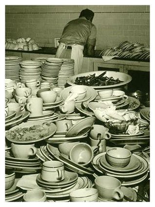 black and white photo of a man washing a huge pile of dishes