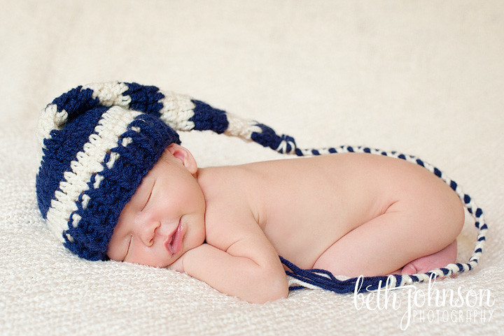 newborn baby boy smiling with navy and cream elf hat