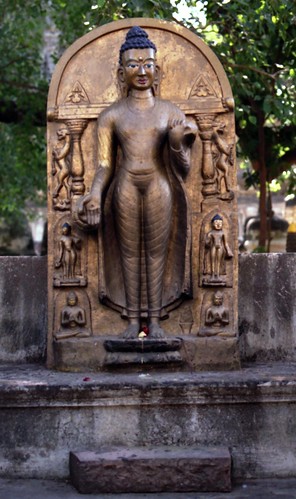 Gold painted concrete statue of standing Buddha in abhaya mudra, holding his robes, with standing lions, 5 Buddhas, columns, offerings on lotus ponce, BodhGaya, H.P., India in 1993 by Wonderlane