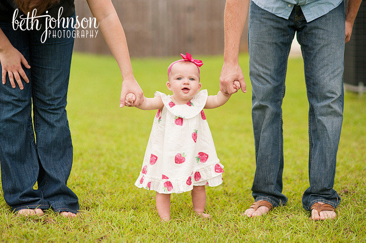 baby girl standing and holding mom and dad hands