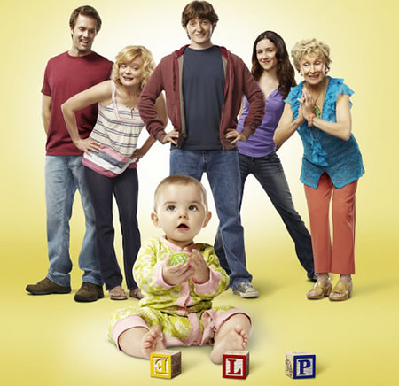cast of the show Raising Hope. A young baby is in the foreground and five adults stand behind her. All are white.
