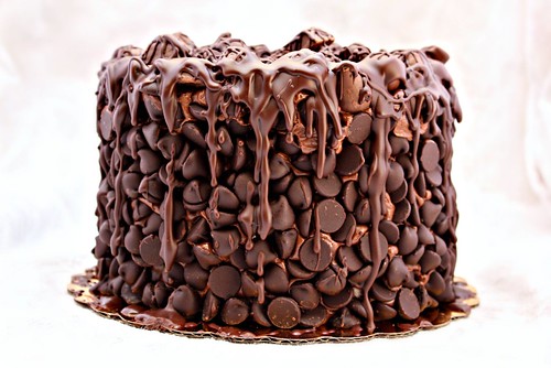 Picture of a multi-tier chocolate cake covered in chocolate chips, candy bars, and drizzled chocolate