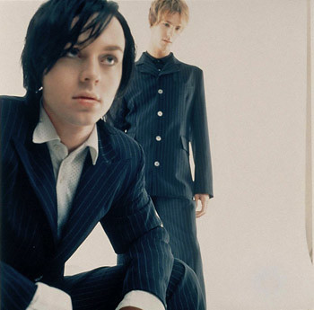 Photo of Savage Garden members in pinstriped navy blue suits and eyeliner, looking away. Both are pale; Darren Hayes, kneeling in the foreground, has dark hair, and Daniel Jones, standing in the background, is blonde.