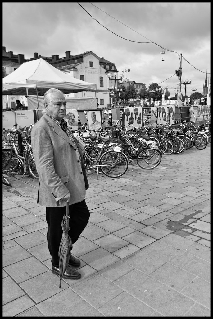 Man with umbrella and book standing in front of bicycles, Stockholm, Sweden
