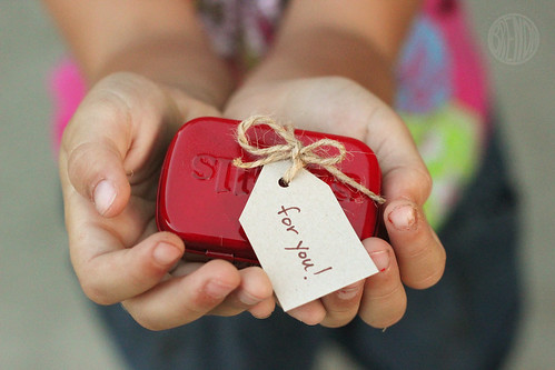 red painted small Altoid can with twine and a gift card in a child's hands 