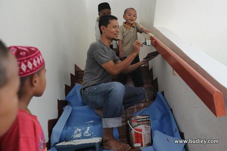2. A 3M Seremban employee painting the staircase railing while the kids look on in amusement.