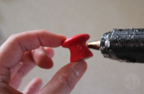 hot glue gun adding glue to red painted wooden knob 