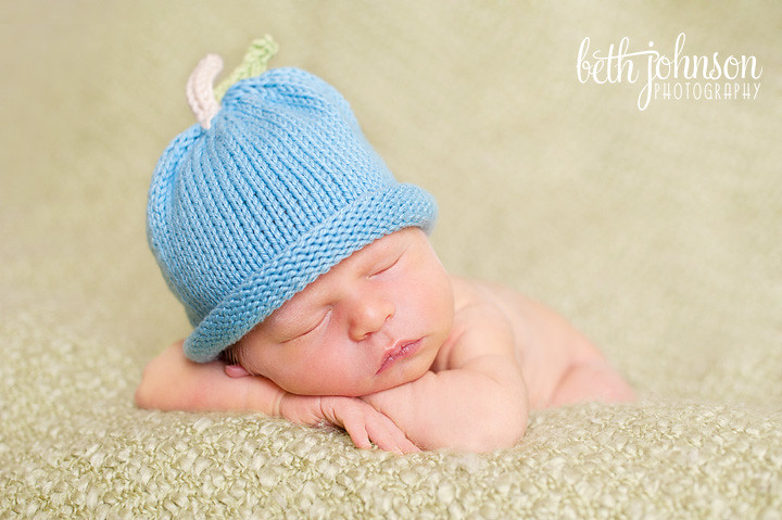 newborn boy in blueberry hat on green blanket