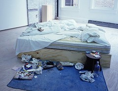 a bed in the middle of a room with stuff strewn around the edges