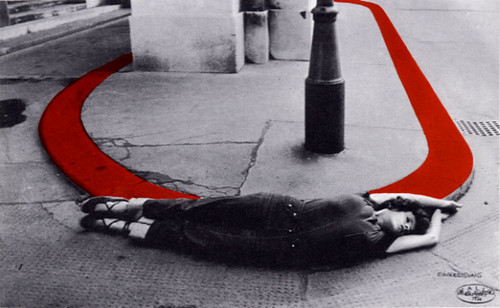 black and white photograph of a woman lying on the ground next to a red half-circle