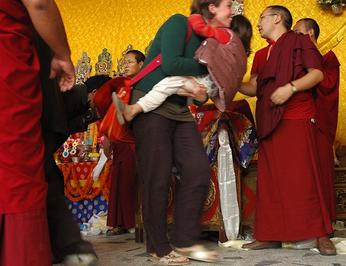 Happy woman carrying a child after getting the long life blessing, running though the line, senior monks keep it moving, Tharlam Monastery of Tibetan Buddhism, Lamdre, Boudha, Kathmandu, Nepal by Wonderlane