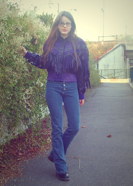 Purple fringed leather jacket, high-waisted blue jeans, colorful necklace as headband.