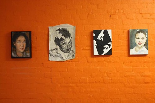 orange gallery wall with four paintings of women hanging on it