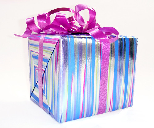 Gift box wrapped in silver paper with purple, blue and green stripes and a magenta bow